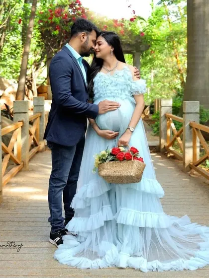 This light blue ruffled gown creates a dreamy, fairytale look, perfect for a romantic couple's maternity shoot. The soft color and delicate ruffles add a touch of elegance, seen here in a beautiful outdoor park setting.