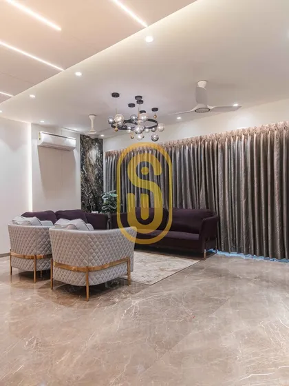 A wide-angle view of the living room, emphasizing the expansive marble flooring and the sophisticated lighting design. The combination of a central chandelier and linear ceiling lights provides layered illumination.