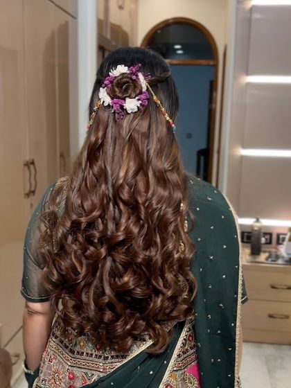 A look at the back of her hair, showing the detailed floral hair accessory and the long, voluminous curls. A perfect hairstyle for any traditional Indian wedding event.