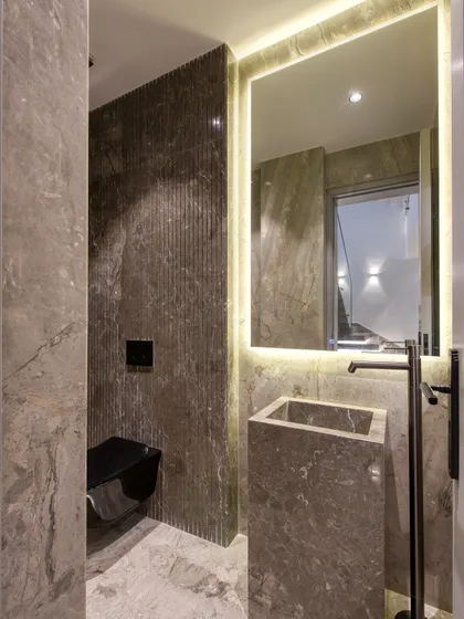 A duplicate of image 8, this powder room showcases a freestanding stone sink and a wall-mounted toilet. The combination of smooth and fluted stone textures adds depth and interest.