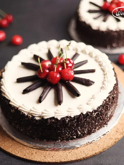 A classic Black Forest Cake, decorated with fresh cream, chocolate shavings, and bright red cherries. This timeless German dessert has been a favourite at our bakery for decades.