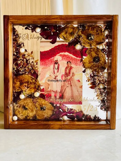 This 10-inch teakwood frame showcases a couple's wedding garland preserved with care. The flowers are arranged to create a beautiful border around their photo, making it a perfect wedding gift.