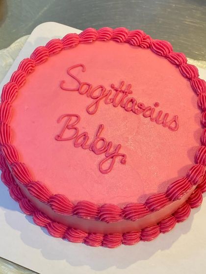 A vibrant pink cake for a "Sagittarius Baby." The simple design with elegant script and a piped border is a stylish way to celebrate a birthday.