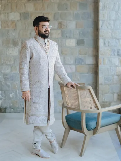 A classic portrait of the groom in his elegant ivory sherwani, standing with a poised and confident look.