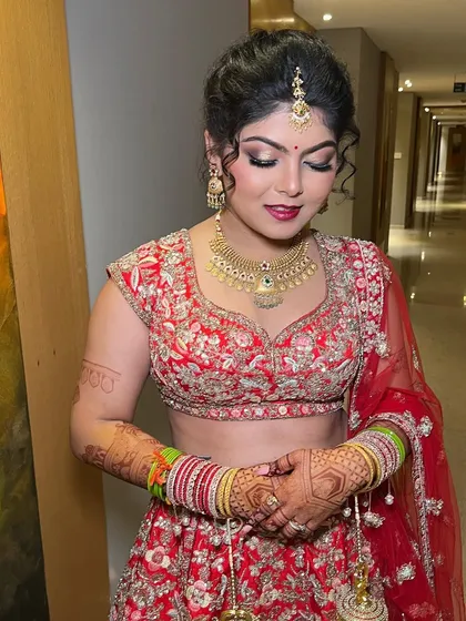 A beautiful bride in her red lehenga, looking down with a gentle smile. The makeup features a soft smokey eye and a deep red lip.