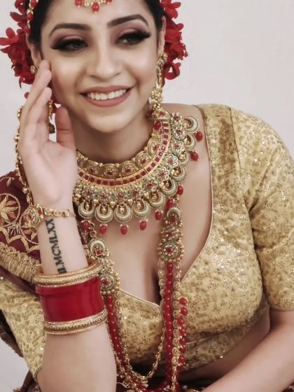 A smiling bride wearing a red and gold jewellery set, complete with a long rani haar. The flowers in her hair add a fresh, beautiful touch.