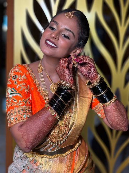 A happy, candid moment. The bride's joyful expression while putting on her earrings shows how comfortable and beautiful she feels in her complete Muhurtham look.