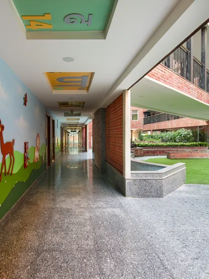 A corridor at a school opens up to a green courtyard, with a colorful mural on the wall. This design choice seamlessly connects the indoor learning environment with nature and art.
