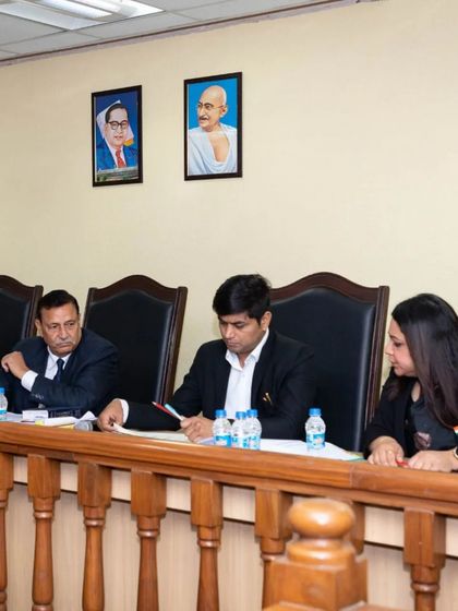 On the judging panel, listening intently to a student's argument. My role is to test their knowledge and reasoning, preparing them for the rigors of a real courtroom.