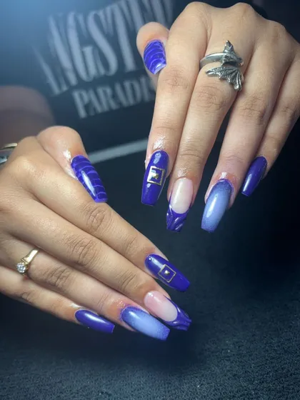 A bold set of long, coffin-shaped nails in a vibrant royal blue, with ombre, textured, and negative space accents.