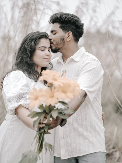 A tender embrace in a field, with the groom kissing the bride's forehead as she holds a bouquet of yellow flowers.