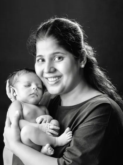 A beautiful black and white portrait of a mother smiling कंटेंटली while holding her sleeping newborn.