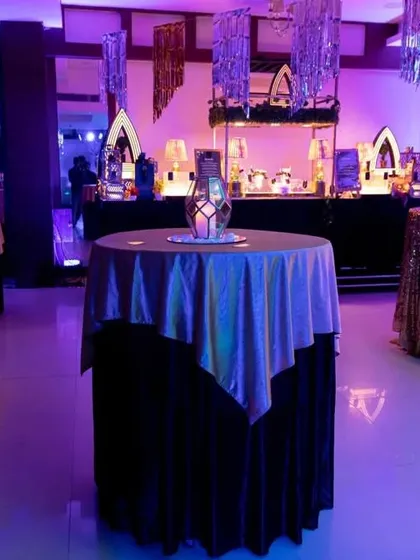 The cocktail lounge area, with high-top tables covered in shimmering linens. The purple uplighting and hanging silver tassels create a glamorous and party-ready atmosphere.