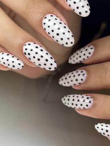 A full view of a playful black and white polka dot manicure. The clean, uniform dots on the milky white base create a striking and graphic look.