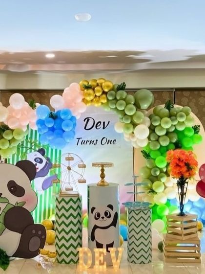 A cute panda theme for a first birthday party. This setup uses large panda cutouts, a multi-colored balloon garland, and custom-wrapped pedestals to match the green and white color scheme.