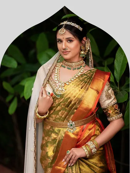 This bride embodies timeless grace in her olive green silk saree, paired with an exquisitely embroidered blouse and a sheer white veil, blending tradition with a hint of contemporary style.
