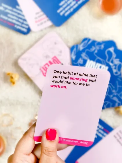 A lifestyle shot for a game night. A hand holds up one of the game cards, with popcorn and drinks scattered in the background, creating a fun and relatable scene.
