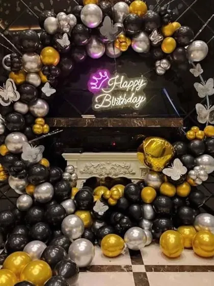 A chic black, gold, and silver balloon arch with a 'Happy Birthday' neon sign, perfect for a stylish celebration.