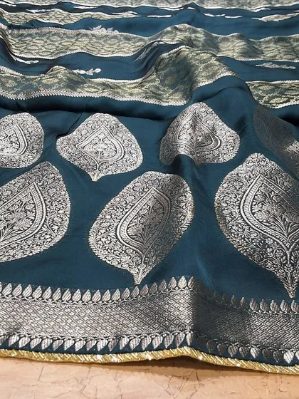 A close-up of a teal green soft silk saree with large paisley motifs in silver zari. The rich color and lustrous fabric make it a luxurious choice for any special occasion.