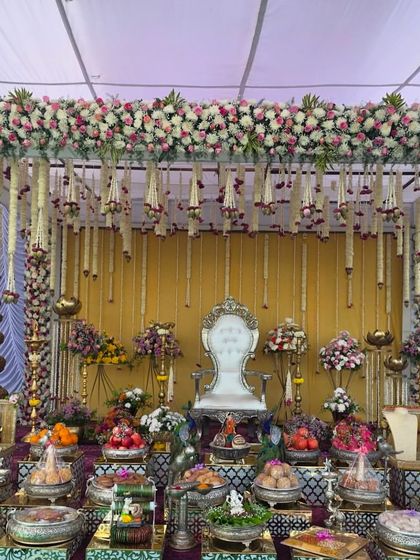 A full view of an elegant outdoor Seemantham ceremony. The stage is covered by a floral canopy with hanging garlands, and the front is beautifully arranged with traditional offerings and a silver throne.