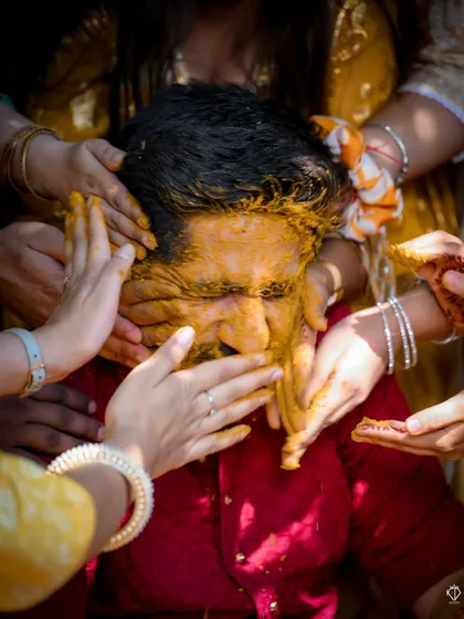 The groom gets lovingly covered in Haldi by his family. This shot is all about the energy and tradition of the moment.