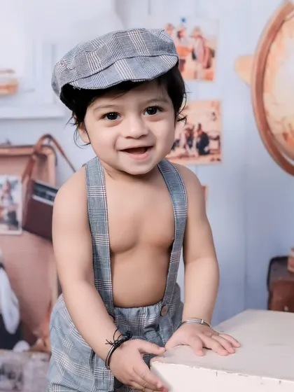 A happy, smiling toddler in a newsboy cap and suspenders, fitting the vintage theme perfectly.