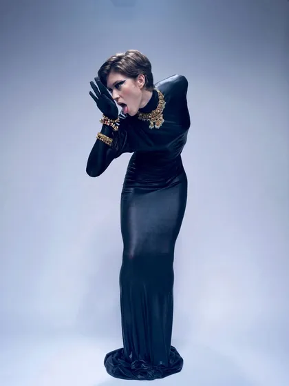 A dramatic, full-body pose for a high-fashion shoot. The look features a bold, graphic black eyeliner and a sculpted pixie haircut, creating a powerful and androgynous silhouette.
