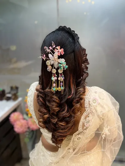 A beautiful half-up, half-down hairstyle with voluminous curls, adorned with a stunning statement floral accessory.