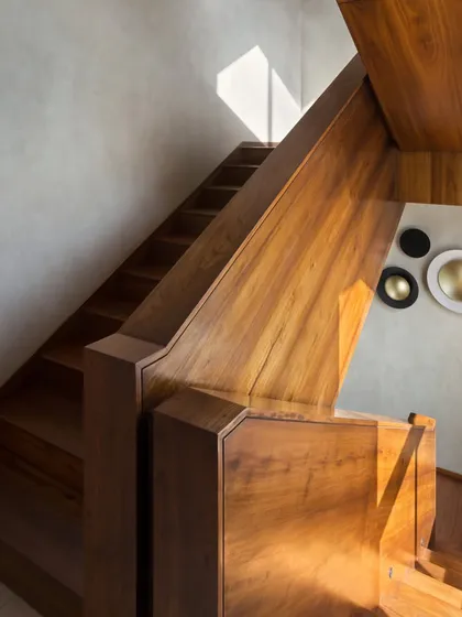 The dog-legged staircase in the House of Terraces is clad entirely in rich Burma teak, serving as a warm, central spine connecting all floors of the villa. The play of sunlight on the wood highlights its natural grain and beauty.