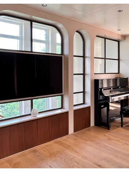 On an upper floor of the villa, the arched window motif frames a media and music corner. The design cleverly integrates a television and provides a niche for a piano, making it a functional and aesthetically pleasing family space.