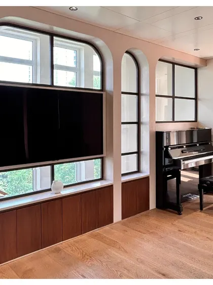 On an upper floor of the villa, the arched window motif frames a media and music corner. The design cleverly integrates a television and provides a niche for a piano, making it a functional and aesthetically pleasing family space.