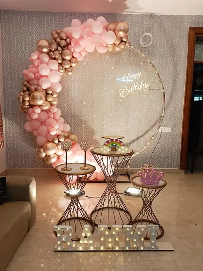 A beautiful half-ring balloon decoration in pink and rose gold, with fairy lights and personalized marquee letters on the floor.