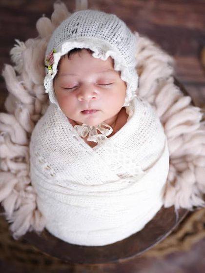 A perfectly swaddled newborn in a white bonnet and wrap, looking so peaceful. I ensure every baby is posed safely and comfortably.