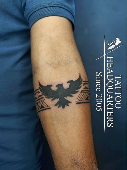 An armband tattoo featuring a solid black silhouette of a bird with its wings spread, integrated into a tribal pattern.