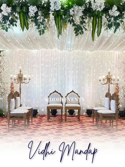 A full view of the pristine white Vidhi Mandap, showcasing the symmetrical arrangement of traditional chairs, candelabras, and cherry blossom trees against a sparkling backdrop.