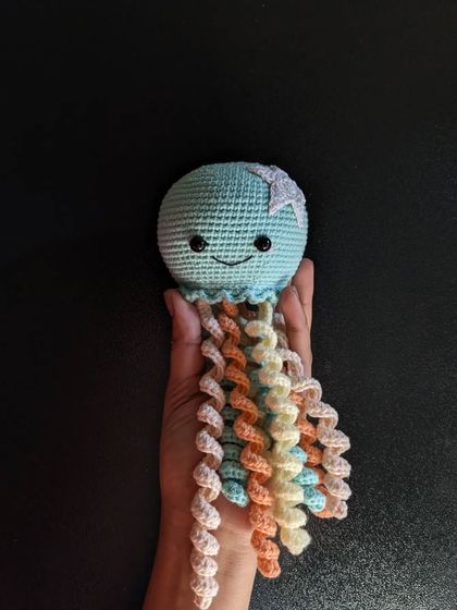 A cute jellyfish amigurumi with a happy smile and long, curly tentacles in pastel colors.