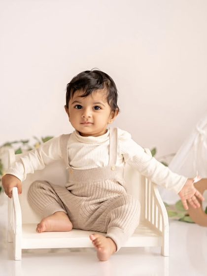 A happy baby boy sitting on a tiny bed in his minimalist boho first birthday setup.