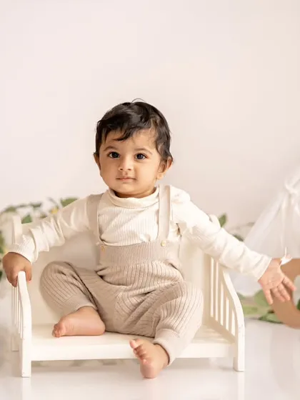 A happy baby boy sitting on a tiny bed in his minimalist boho first birthday setup.