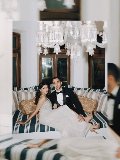 A high-fashion, paparazzi-style portrait. The couple poses with effortless glamour under the chandeliers, creating an image that is both sophisticated and full of personality.