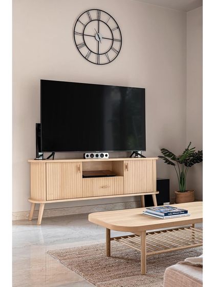 Opposite the concrete seating is a minimal media console with elegant fluting details. The light wood finish keeps the room feeling open and sophisticated while neatly storing all electronic devices.