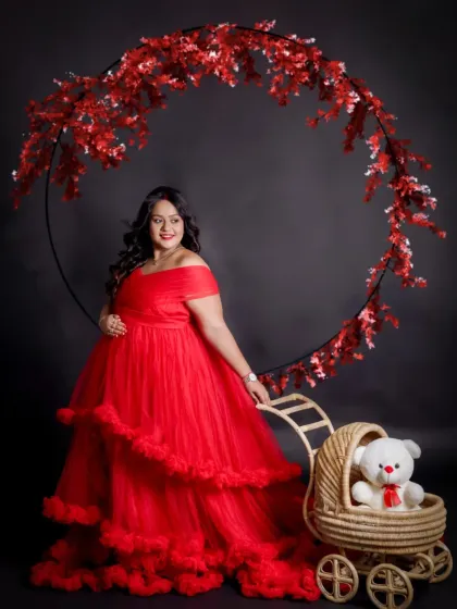 A playful and happy solo shot. The mom-to-be stands with a teddy bear in a pram, framed by a red floral hoop, perfectly capturing the excitement of waiting for the baby.