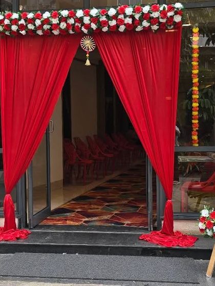A traditional entrance decoration for a baby shower (Seemantham), with red drapes, floral arrangements, and a personalized welcome sign.