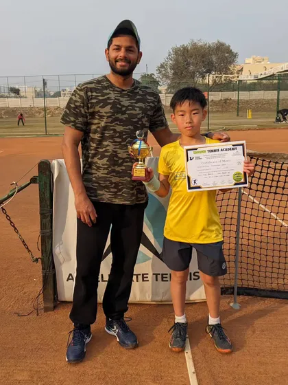 Toshi with his coach and his U14 doubles finalist trophy. Competing against older players is key to accelerating development.