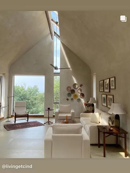 The living room of the 'Wildgrass' home in Coonoor. A high, vaulted ceiling with a narrow skylight draws the eye upwards and fills the space with a soft, changing light, while a large window frames the view of the forested valley.