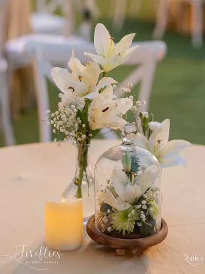 A simple and elegant centerpiece featuring white lilies, with one bloom captured under a glass cloche, adding a touch of modern sophistication.
