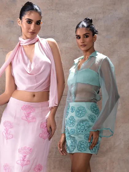 Two models showcasing contemporary festive wear. The makeup is clean and modern, with a focus on sharp, defined eyes that complement the stylish silhouettes of the outfits, perfect for a fashion-forward wedding guest or bridesmaid.