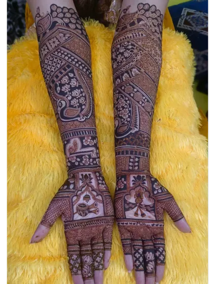 A full-coverage bridal mehndi with a prominent paisley peacock design. The rest of the arm is filled with delicate floral vines and checkerboard patterns, creating a rich and dense look.