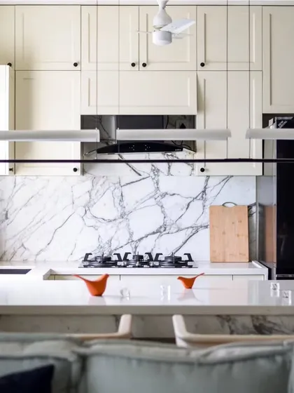 The kitchen is a culinary oasis with a classic European touch. White quartz countertops and a Statuario marble backsplash create a clean, pristine canvas, complemented by classic European-style cabinets.