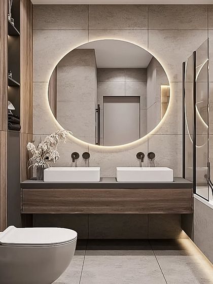 This contemporary bathroom features a double vanity with two vessel sinks and a large, backlit round mirror. The wood-finish cabinets and grey tiles create a warm, spa-like atmosphere.