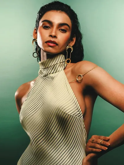 A clean, elegant shot for the Batoki Art jewelry campaign. The focus is on the product and the model's direct gaze, set against a solid green backdrop to make the gold jewelry stand out.